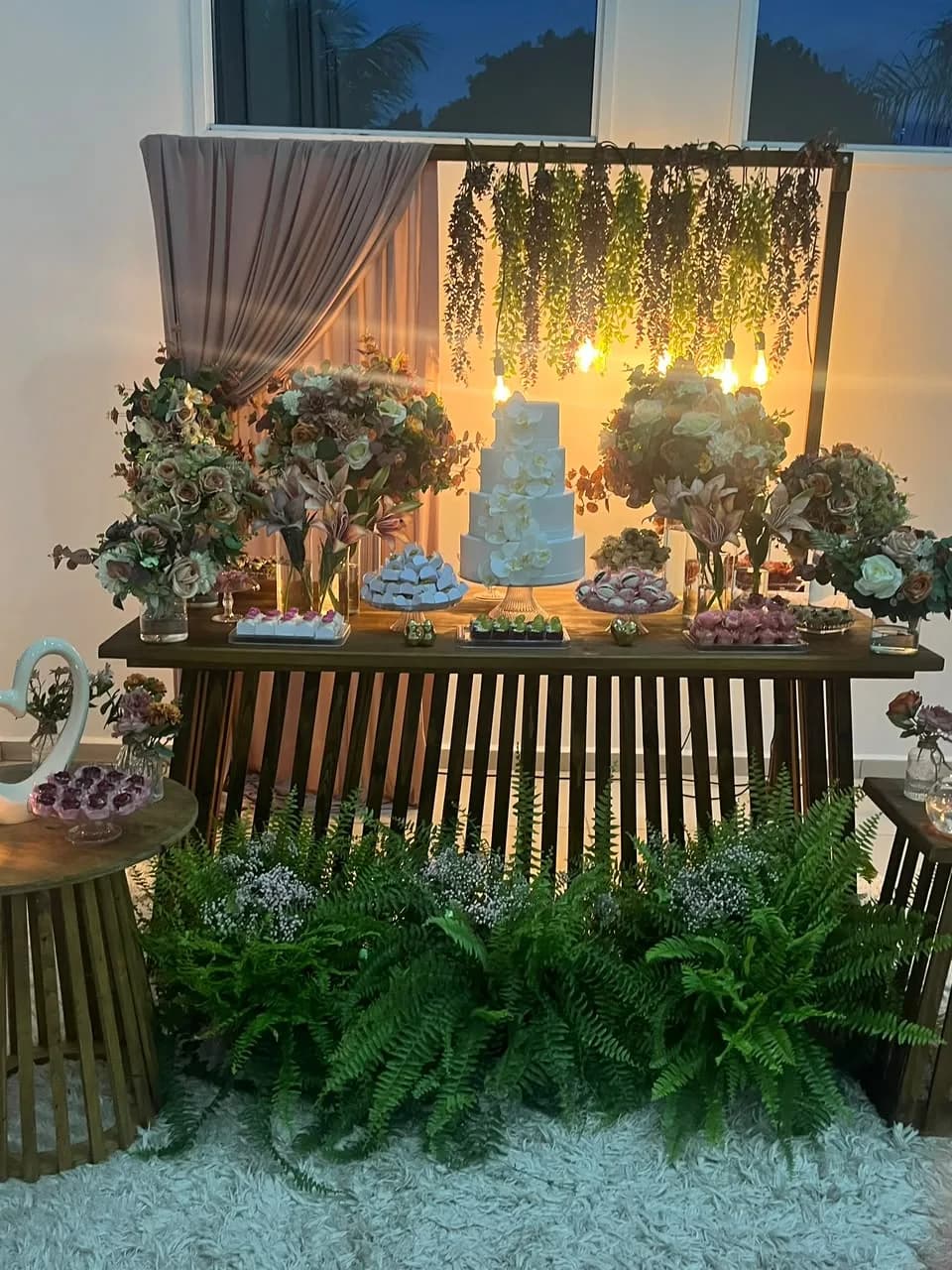 Mesa de doces iluminada com cortina de folhagens pendentes